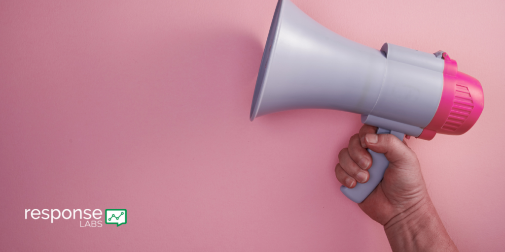 A human hand holds a megaphone against a pink background.