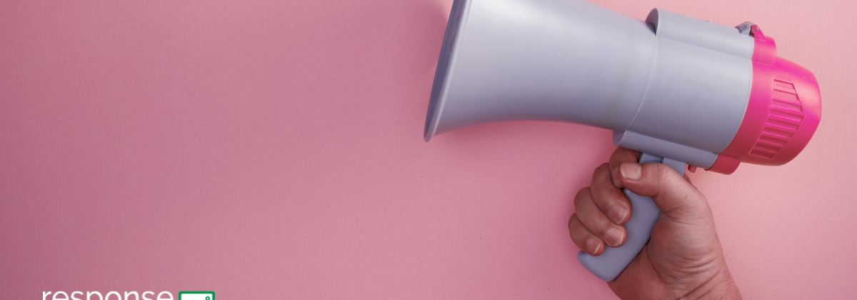 A human hand holds a megaphone against a pink background.